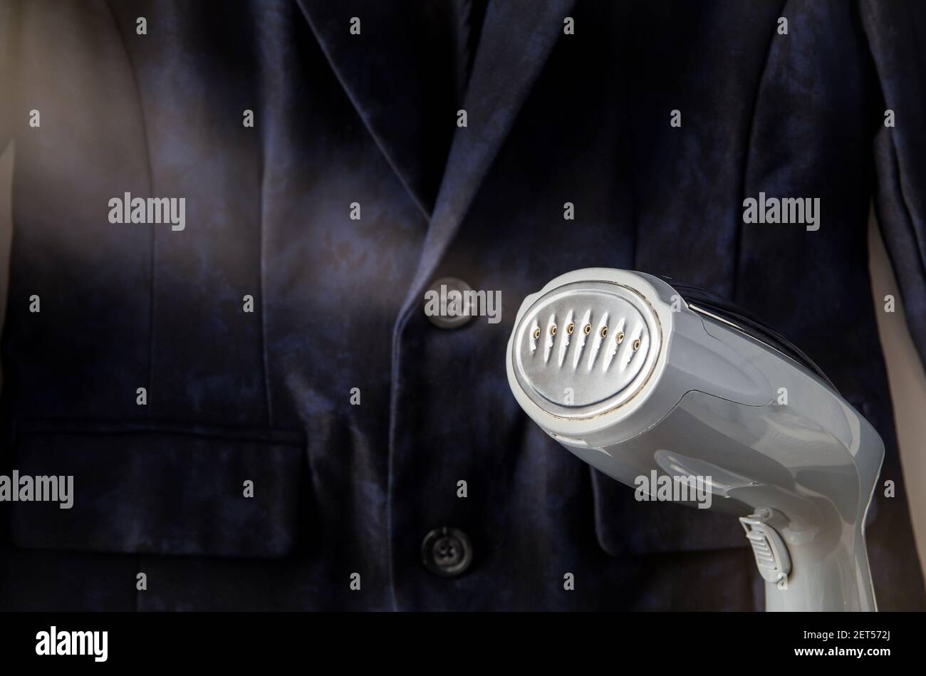 Close up view of small handheld fabric clothing steamer machine, hot steam coming, removing wrinkles. Stock Photo