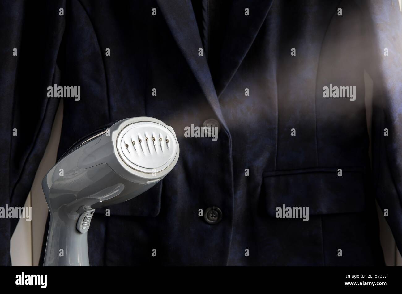 Close up view of small handheld fabric clothing steamer machine, hot steam coming, removing wrinkles. Stock Photo