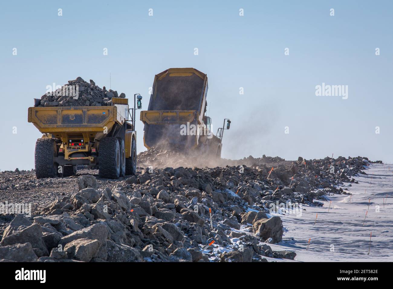 Caterpillar articulated trucks hauling and dumping gravel on Inuvik-Tuktoyaktuk Highway, winter construction, Northwest Territories, Canada's Arctic. Stock Photo