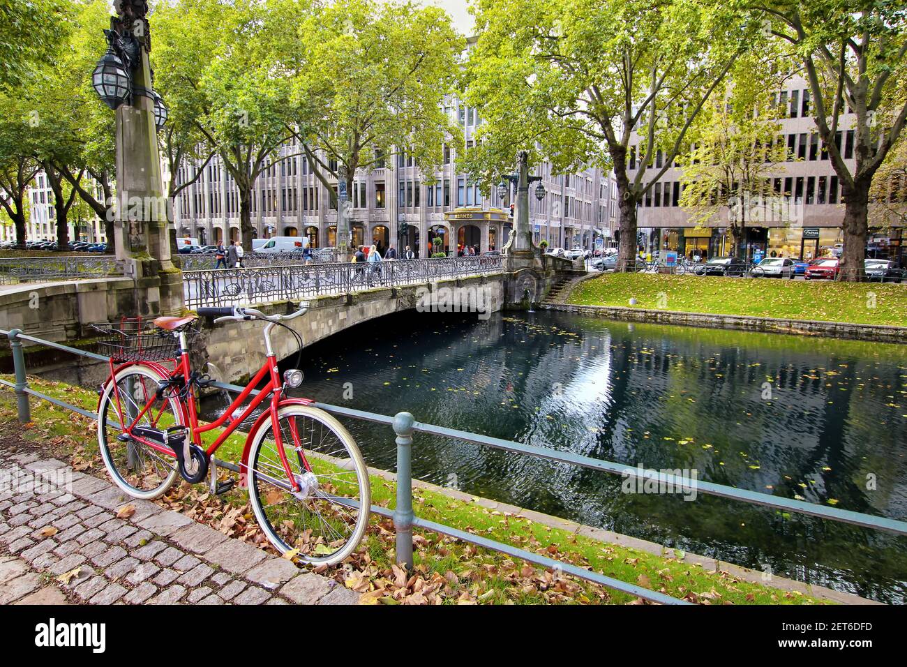 Königsallee is not only a famous shopping boulevard, but also has wonderful green areas. Romantic scenery with red bike at the city canal 'Kö-Graben'. Stock Photo