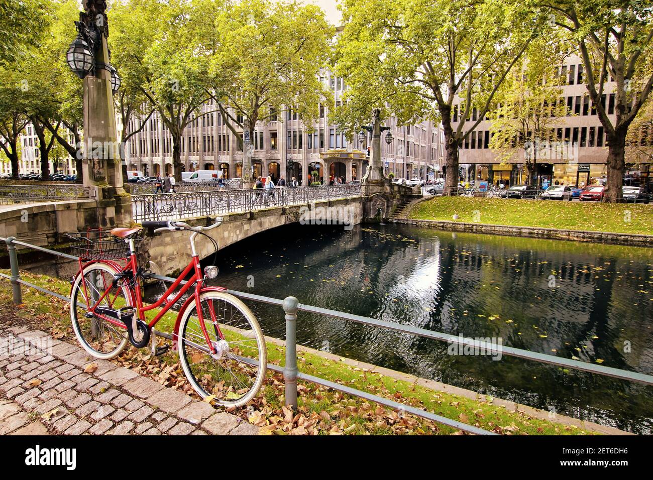 Königsallee is not only a famous shopping boulevard in Düsseldorf, but also has cyclist-friendly green areas. Red bike at the city canal, retro style. Stock Photo