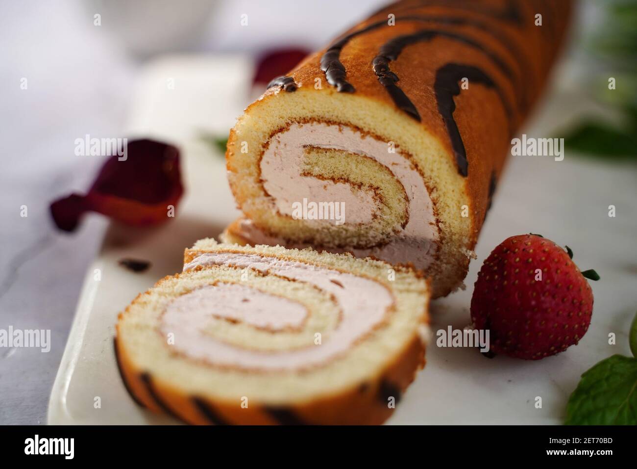 Strawberry Swiss roll or Roulade with cream filling and chocolate drizzle, selective focus Stock Photo