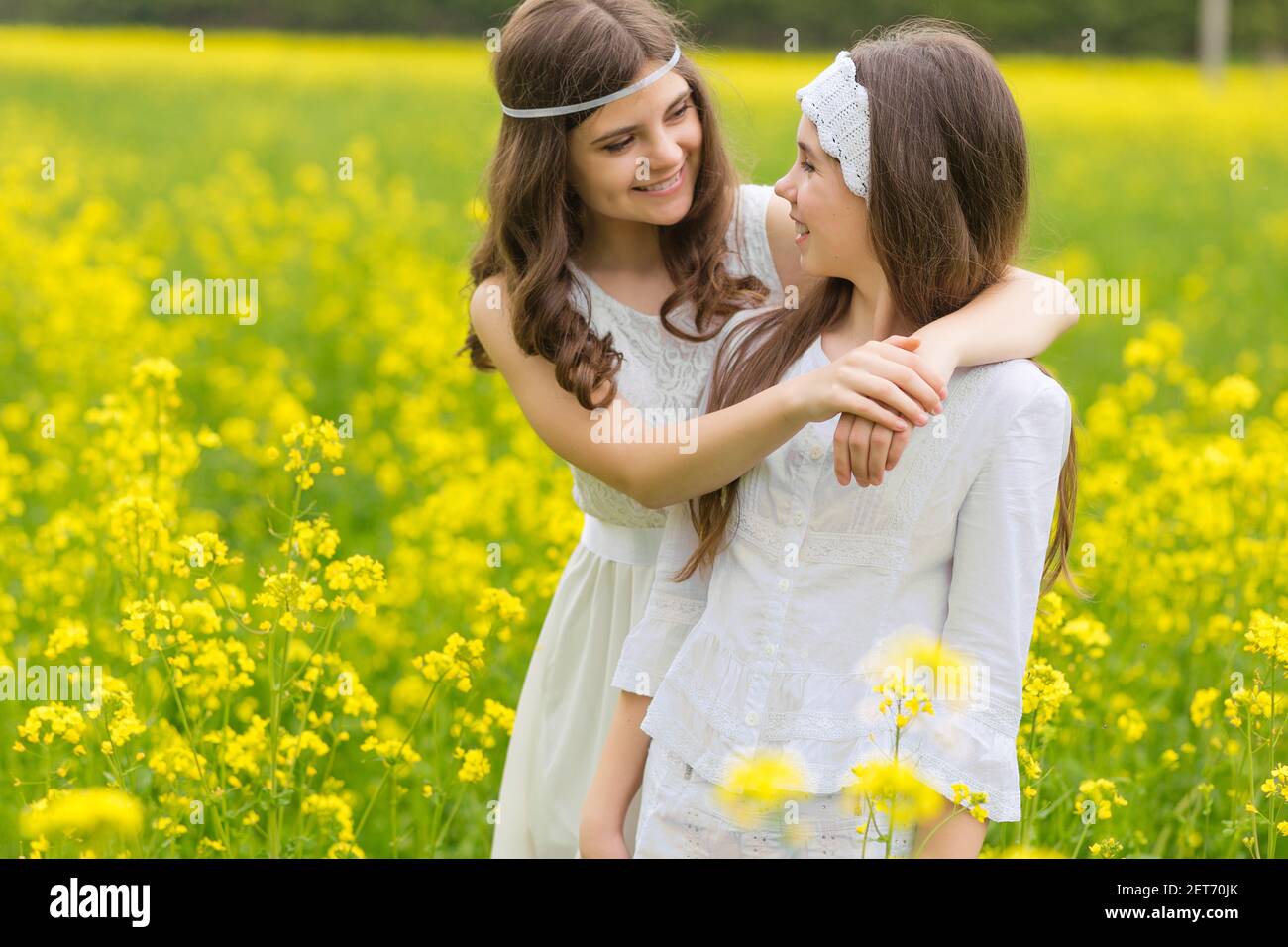 Two girls are walking along a blooming rapeseed field Stock Photo - Alamy