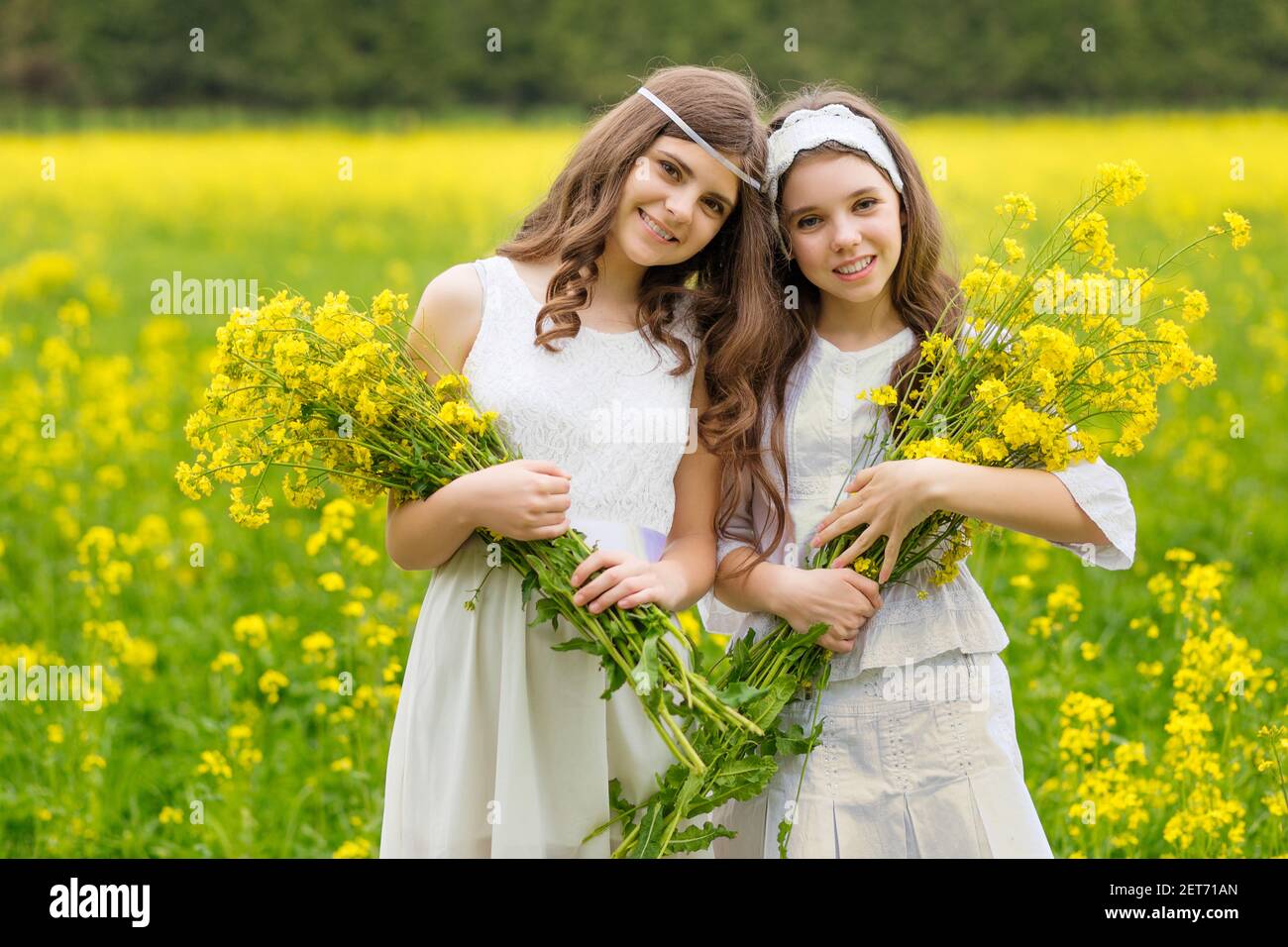 Two girls are walking along a blooming rapeseed field Stock Photo - Alamy