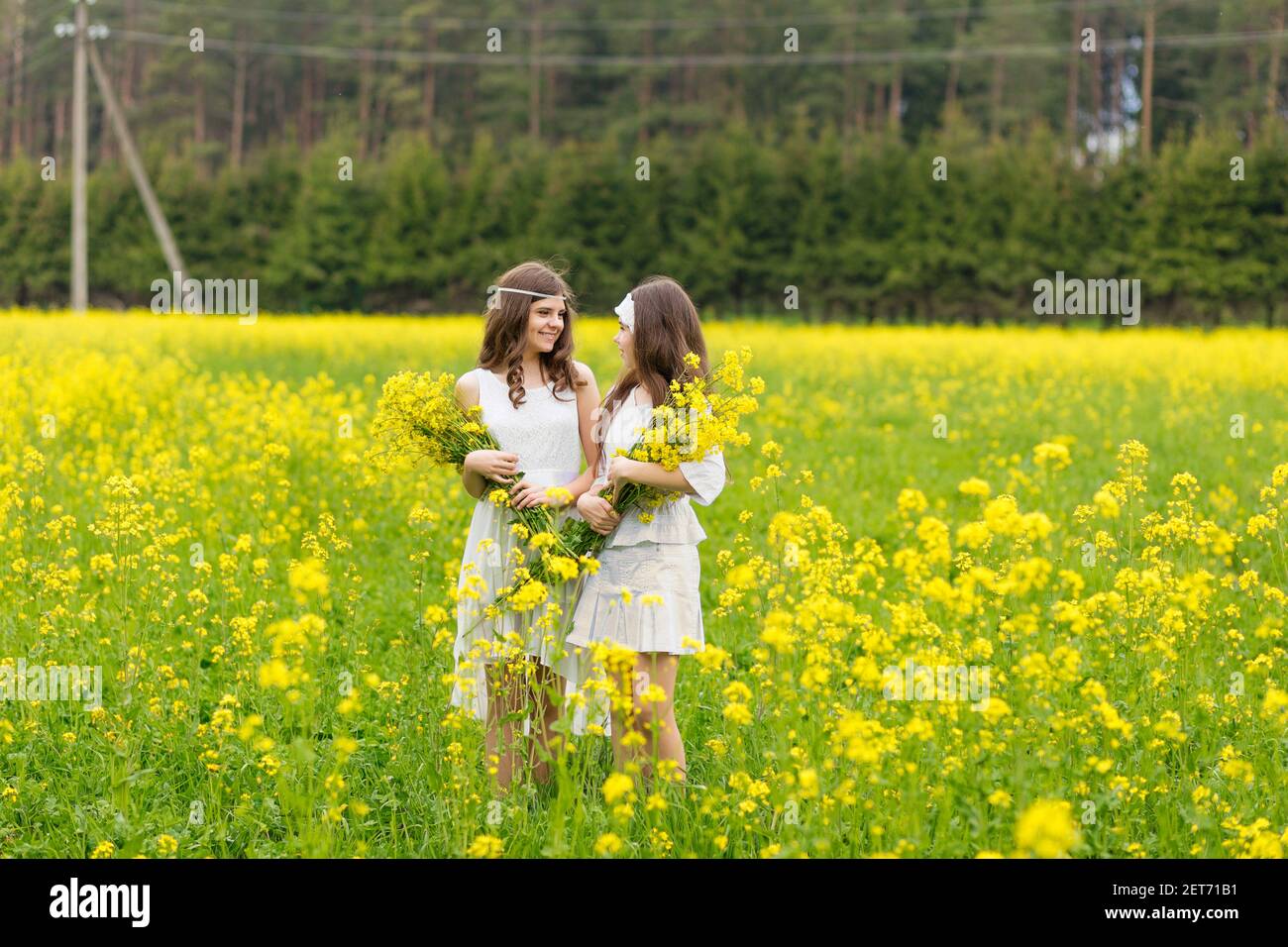 Two girls are walking along a blooming rapeseed field Stock Photo - Alamy