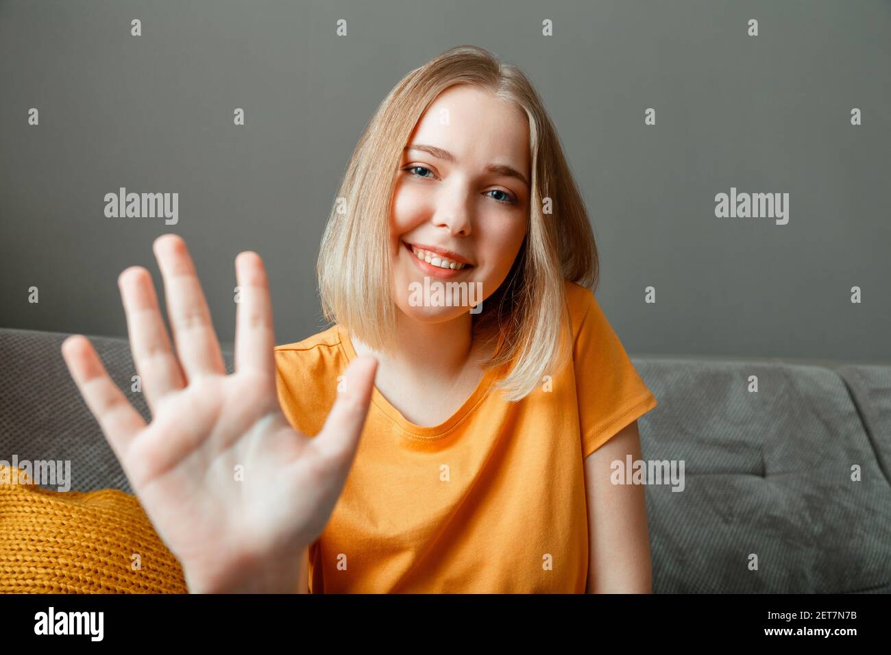 Happy woman portrait wave by hand greeting web camera view. Young beautiful woman talking hi by video call using while sitting on sofa in living room. Stock Photo