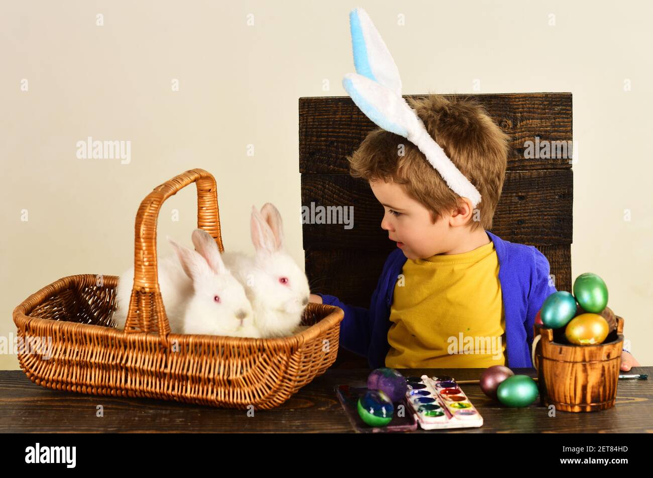Child in bunny ears on Easter day. Cute boy with easters rabbit in basket and eggs. Stock Photo