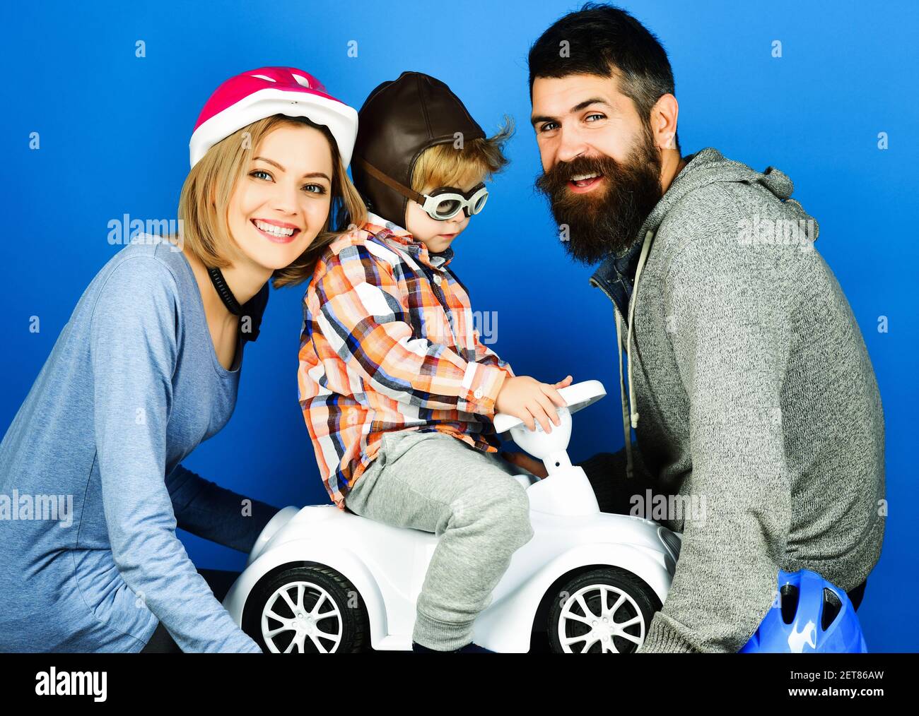 Parenthood. Parenting. Parents play with son in toy car. Happy family in protect sport helmets. Stock Photo