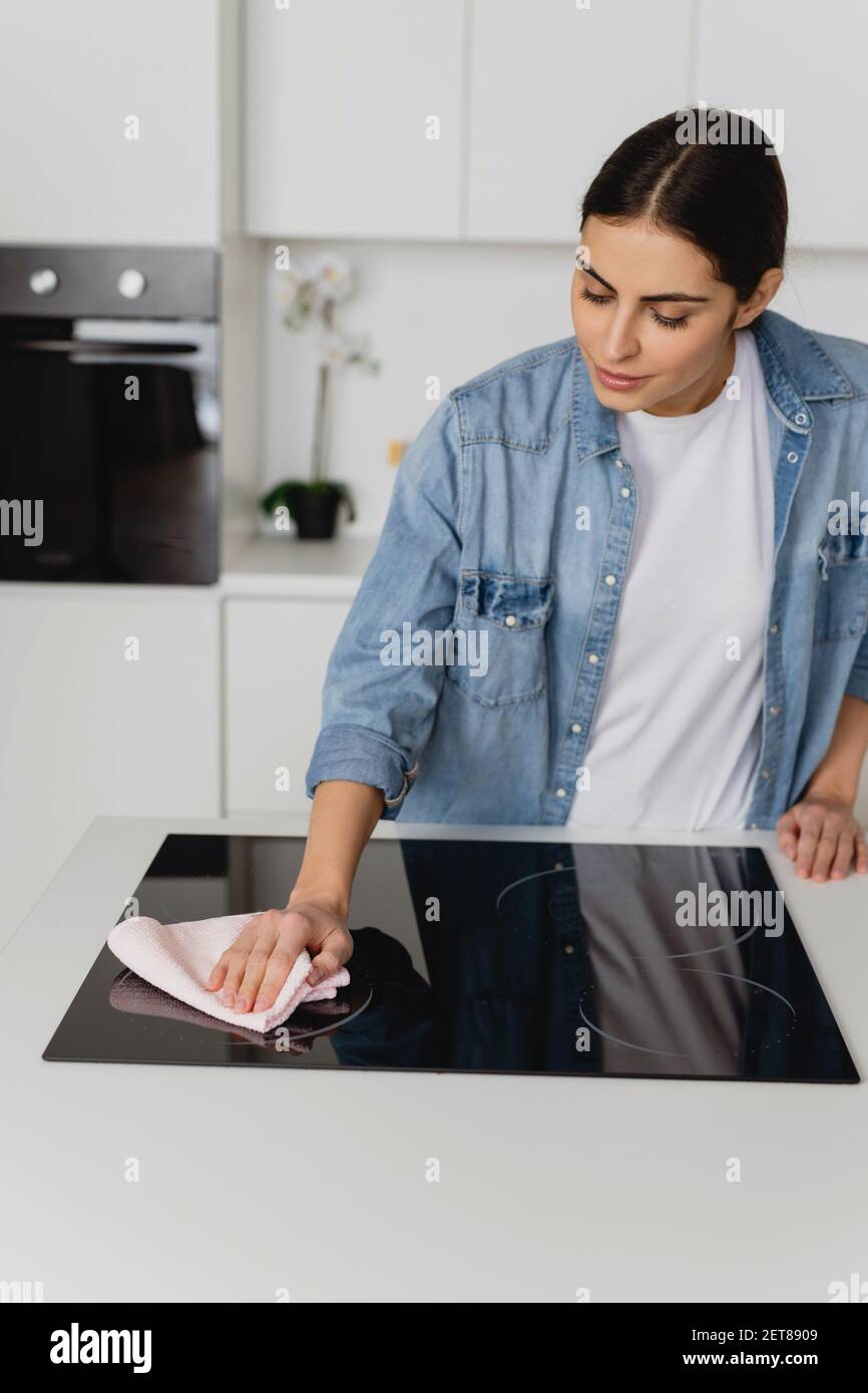 Young woman cleaning a modern black induction hob by rag. Spring cleaning concept. Stock Photo