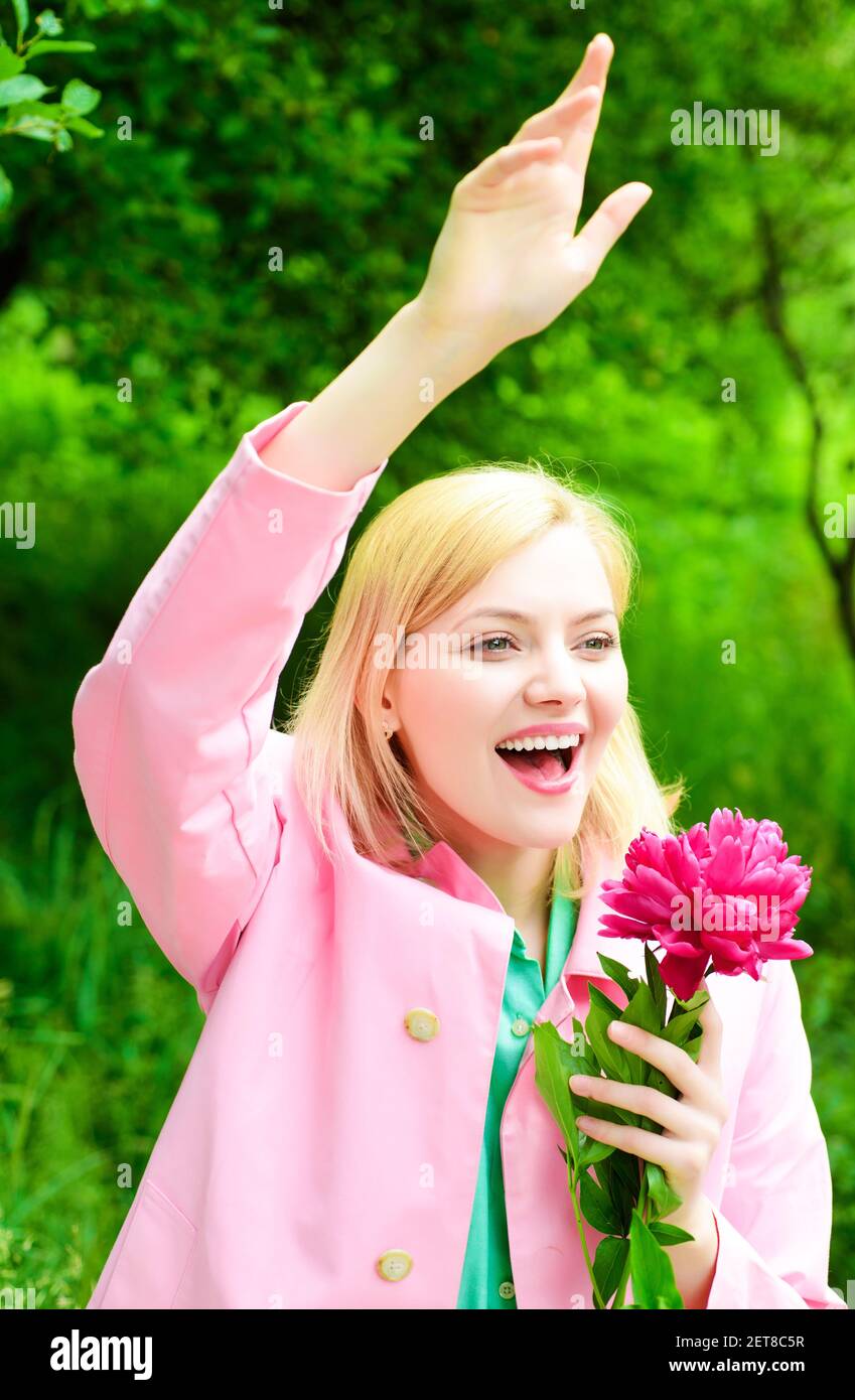 Spring. Smiling woman with peony flower waving hand. Happy girl welcoming to friends Stock Photo