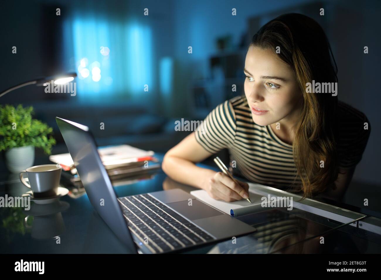 Concentrated woman writing notes checking laptop content in the night at home Stock Photo