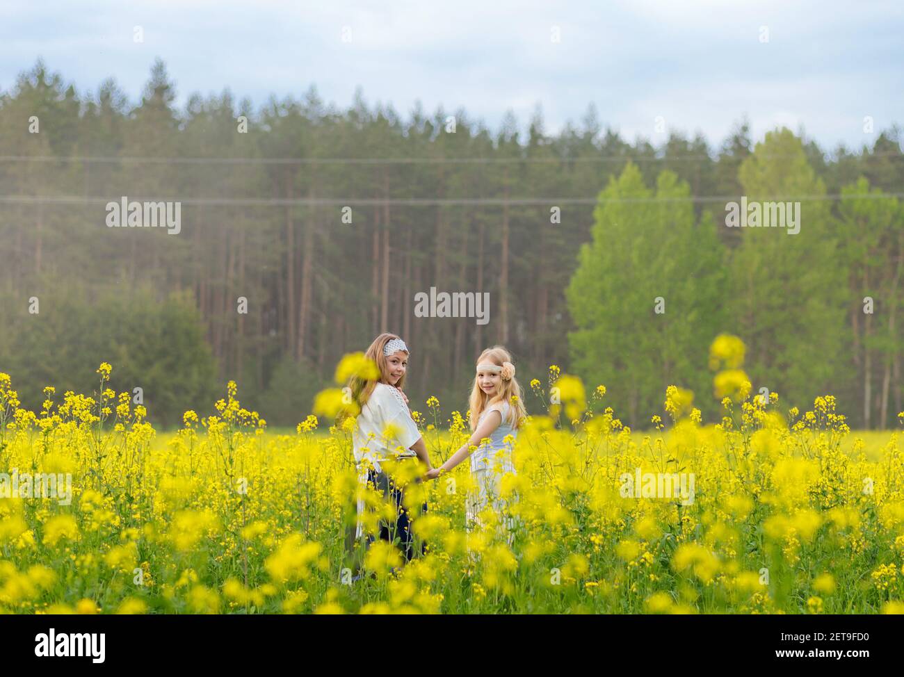 Two girls are walking along a blooming rapeseed field Stock Photo - Alamy