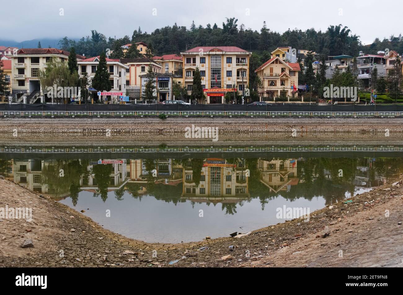 October, 2015 - Sa Pa, Vietnam: Residential buildings reflected in water of city lake. Dirty water with garbage. Low water level. Stock Photo