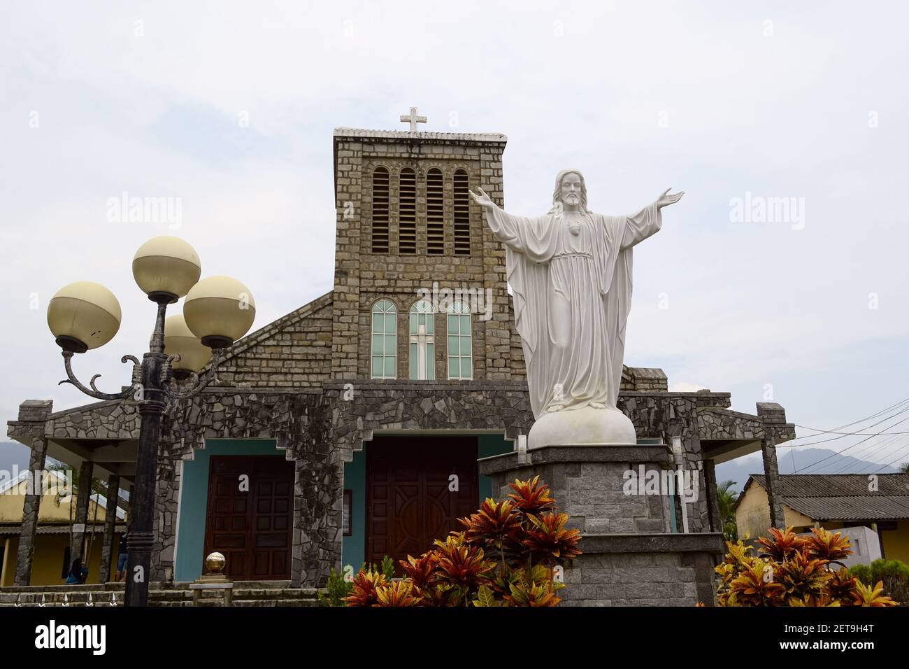 Lang Co, Vietnam - September, 2015: Old colonial catholic church near a beach and white Jesus Christ statue with hands raised up Stock Photo