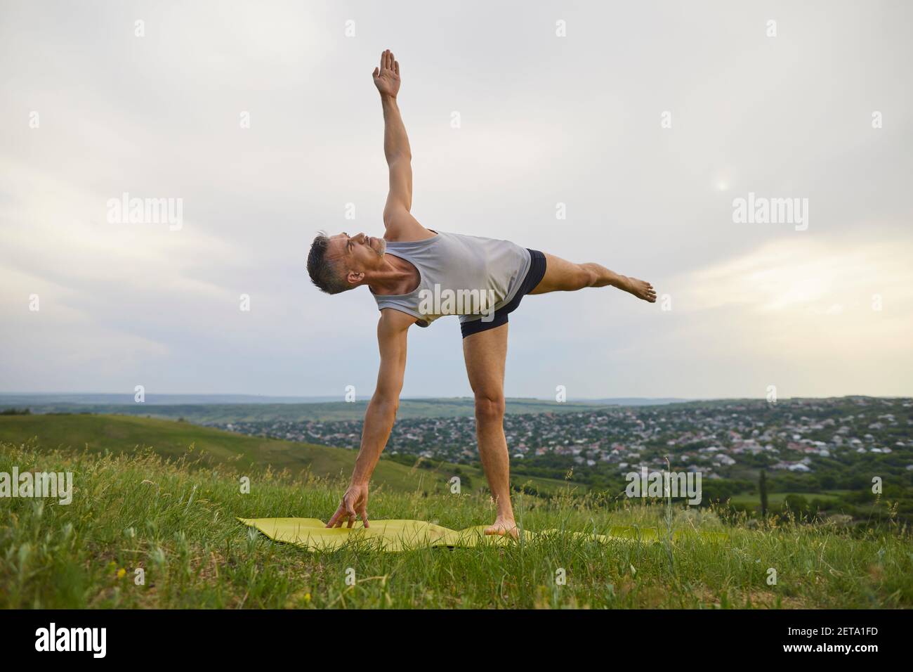 Mature man doing Half Moon pose in countryside Stock Photo