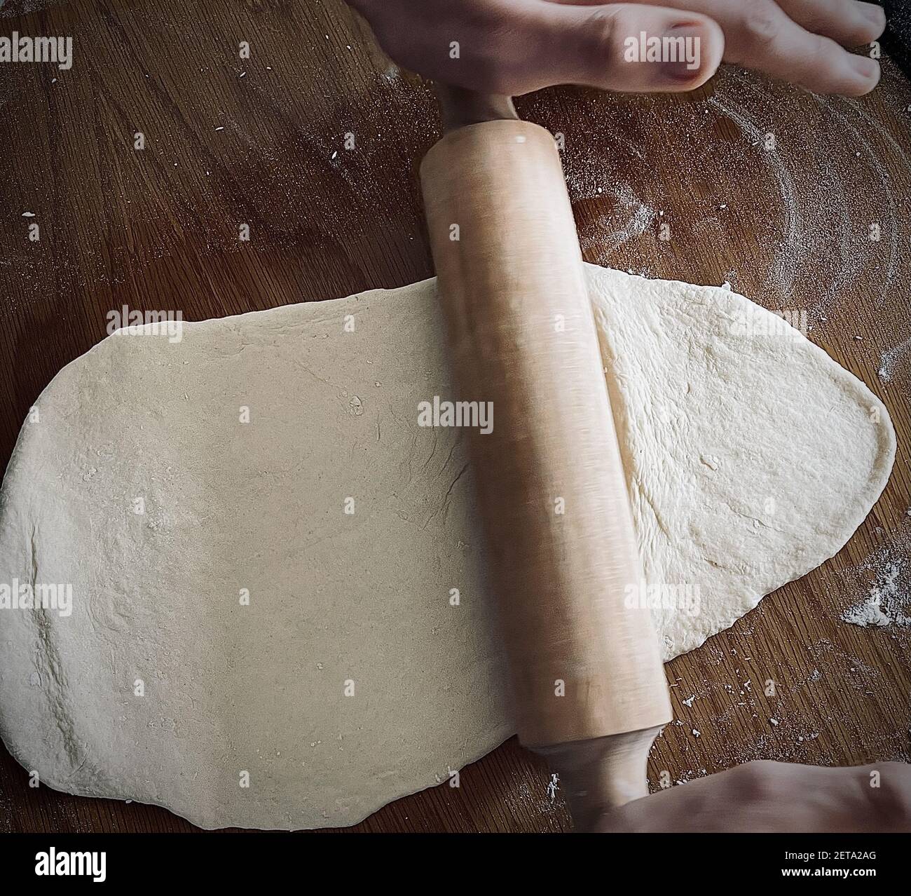 An old woman stretching the dough with a wooden rolling pin on the