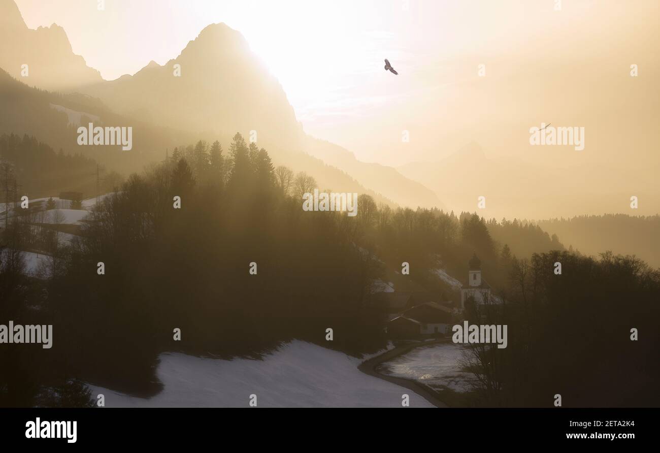 Epic glowing sunset in the mountains with birds circling over church village - sahara dust Stock Photo