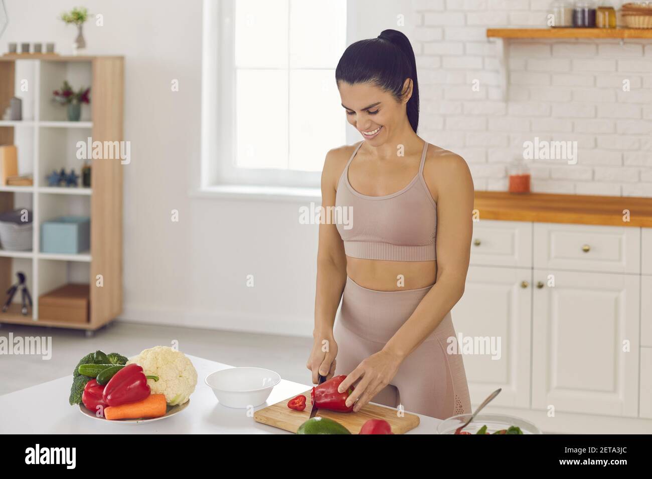 Happy woman standing at table and chopping red peppers for healthy vegetarian salad Stock Photo