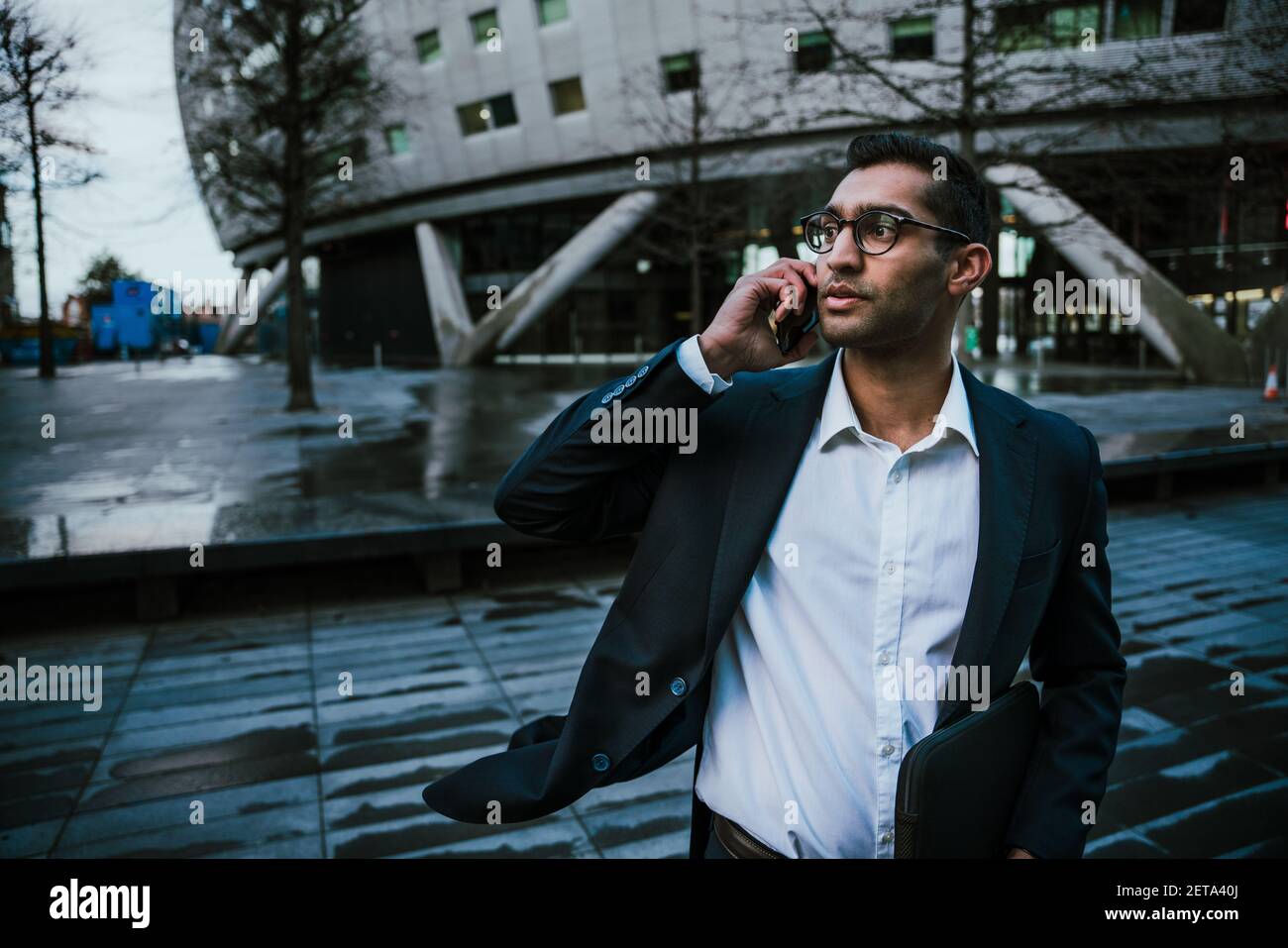 Young mixed race business man standing outside office talking on cellular device Stock Photo
