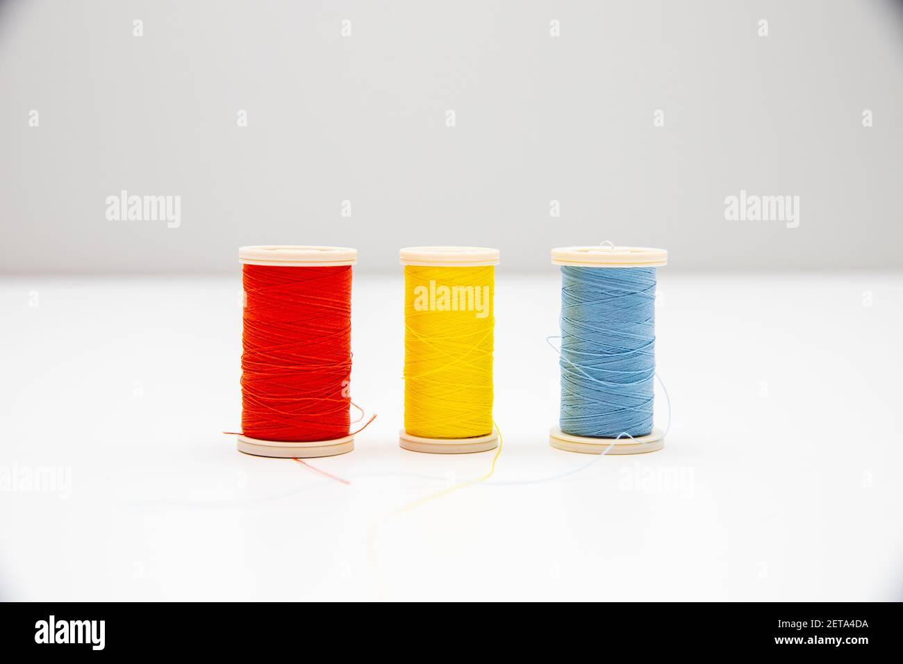 A closeup of red, yellow, and blue thread spools in the light background Stock Photo