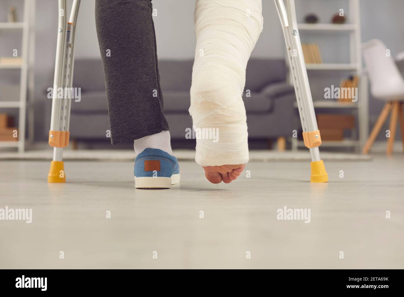 Legs part of young man with broken leg in cast walking with crutches at