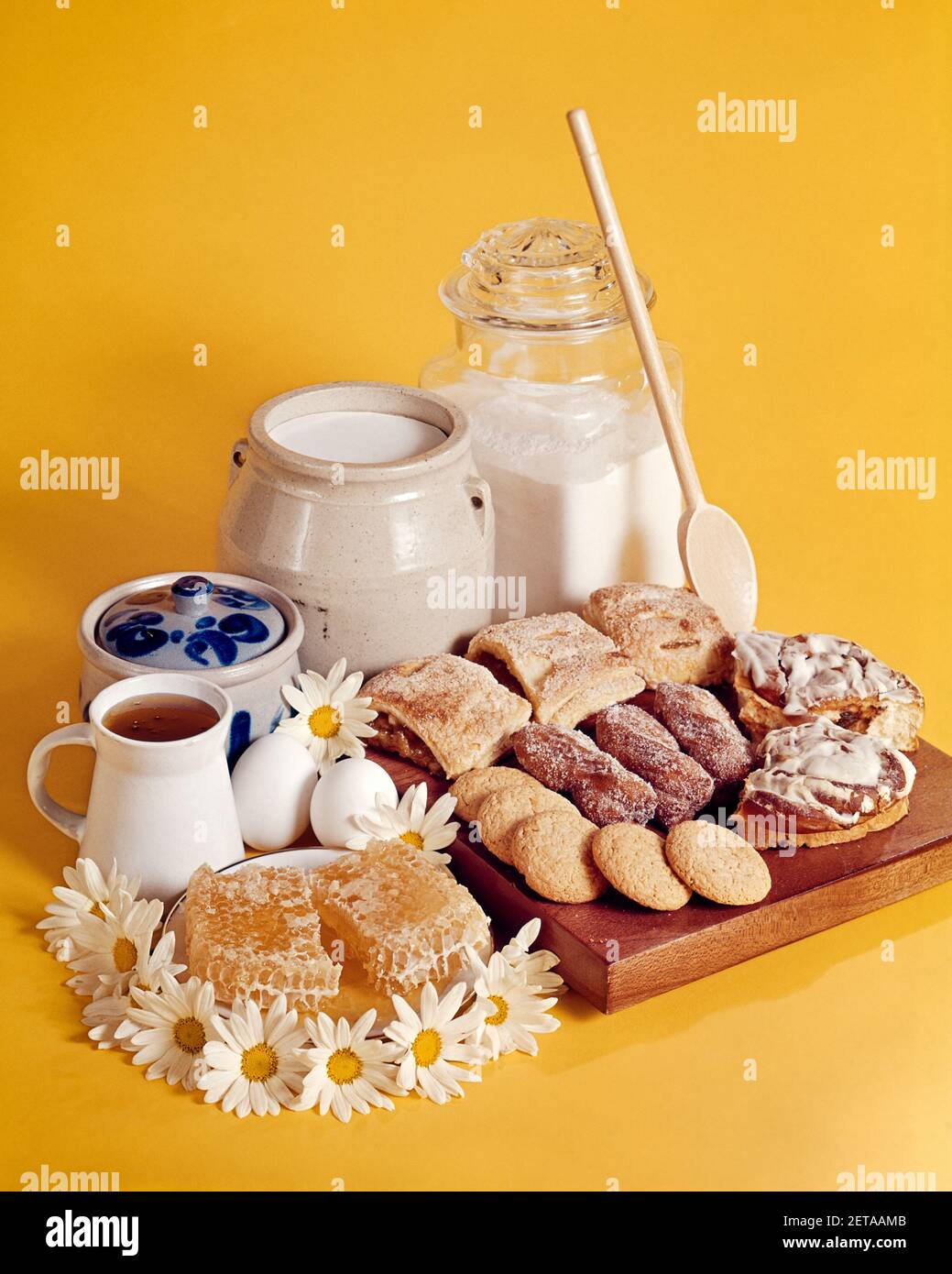 1970s FINISHED BAKED BREAKFAST PASTRIES ON A WOOD BLOCK SURROUNDED BY WOODEN SPOON AND INGREDIENTS FLOUR MILK HONEY EGGS SUGAR - kf8553 PHT001 HARS OLD FASHIONED Stock Photo