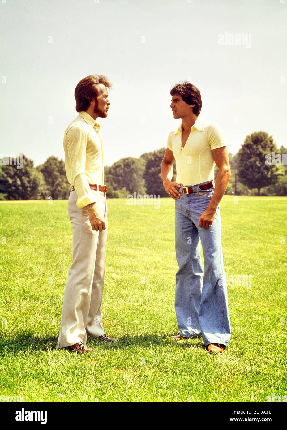 1970s TWO YOUNG MEN WEARING BELL BOTTOM PANTS STANDING ON GRASSY