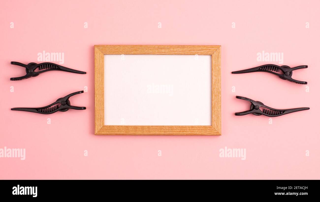 Banner mockup wooden frame flat lay of four black section hair clips of the right and left of the frame template with copy space on pink background. H Stock Photo