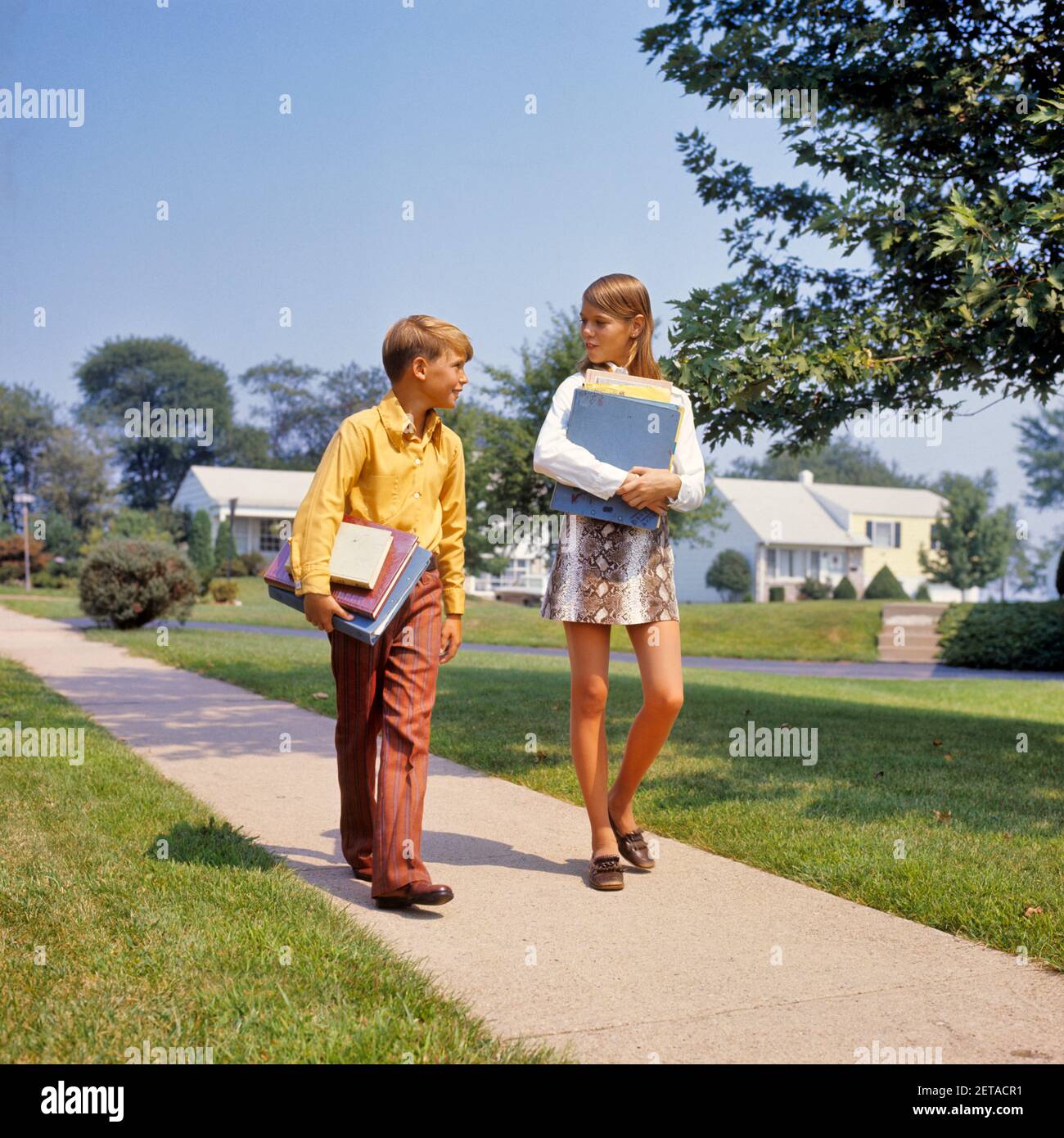 1960s 1970s BOY GIRL ON SIDEWALK WALKING HOME FROM OR TO SCHOOL TALKING CARRYING BOOKS GIRL WEARING FAUX SNAKESKIN MINI SKIRT - ks7526 HAR001 HARS 1 JUVENILE ELEMENTARY STYLE COMMUNICATION FRIEND MINI JOY LIFESTYLE FEMALES HOUSES BROTHERS HEALTHINESS HOME LIFE COPY SPACE FRIENDSHIP FULL-LENGTH RESIDENTIAL MALES BUILDINGS SIBLINGS SISTERS SCHOOLS GRADE HAPPINESS NEIGHBORHOOD HOMES PRIMARY SIBLING CONNECTION FAUX FRIENDLY RESIDENCE STYLISH OR COOPERATION GRADE SCHOOL GROWTH JUVENILES MIDDLE SCHOOL MINISKIRT PRE-TEEN PRE-TEEN GIRL TOGETHERNESS CAUCASIAN ETHNICITY HAR001 OLD FASHIONED Stock Photo