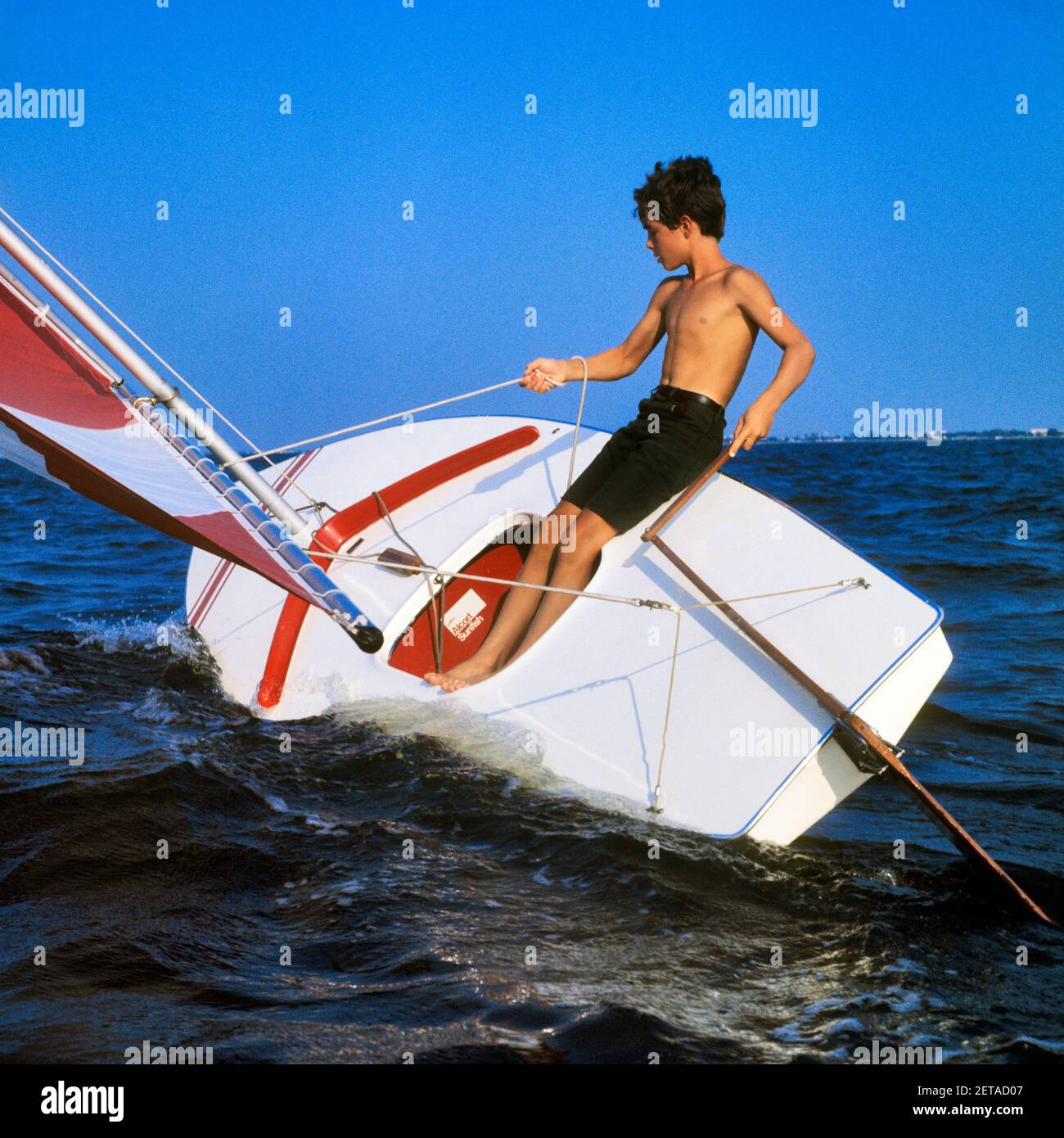 1960s TEENAGE BOY SAILING A RED AND WHITE SUNFISH BOAT HEELING IN THE WIND ON LAKE PONTCHARTRAIN NEW ORLEANS LOUISIANA USA - ky1081 GRD001 HARS ATHLETE RELAXING JOY LIFESTYLE SATISFACTION SHEET ATHLETICS COPY SPACE FULL-LENGTH PERSONS MALES TEENAGE BOY ATHLETIC TRANSPORTATION SKILL ACTIVITY AMUSEMENT PHYSICAL ADVENTURE HOBBY ORLEANS STRENGTH INTEREST AND EXCITEMENT HOBBIES KNOWLEDGE RECREATION PASTIME PLEASURE SUNFISH ATHLETES FLEXIBILITY MUSCLES TEENAGED HEELING JUVENILES RELAXATION AMATEUR CAUCASIAN ETHNICITY ENJOYMENT LA OLD FASHIONED RUDDER TILLER Stock Photo