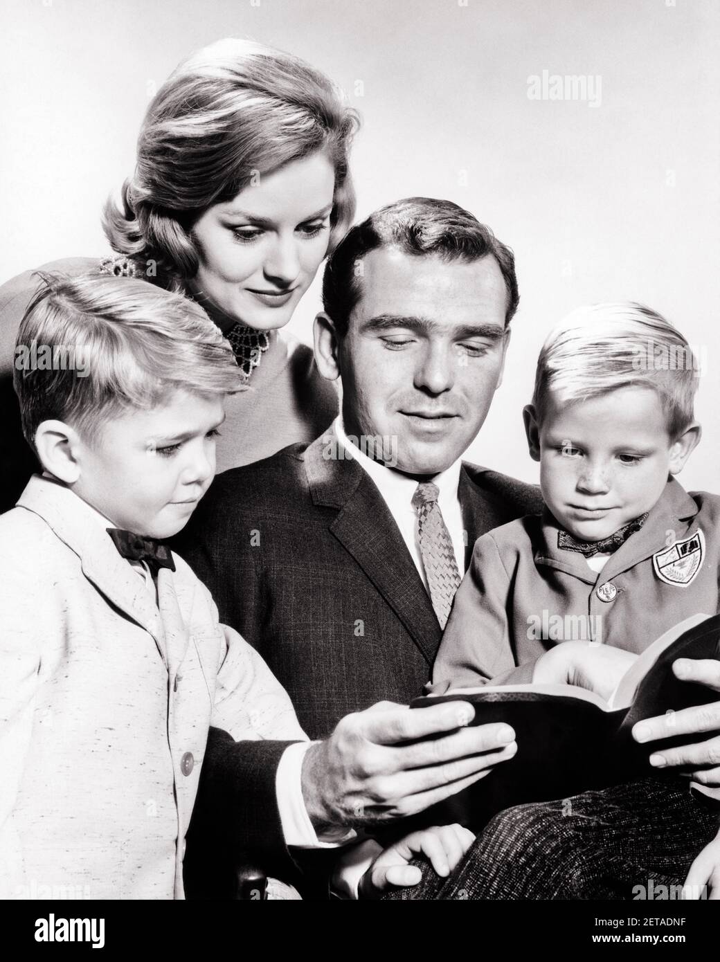 1960s FATHER READING TO HIS WIFE AND TWO SONS FROM A BOOK THE BIBLE - r1832 HAR001 HARS OLD FASHION 1 JUVENILE COMMUNICATION INFORMATION SONS FAMILIES LIFESTYLE SATISFACTION RELIGION FEMALES MARRIED BROTHERS SPOUSE HUSBANDS COPY SPACE FRIENDSHIP HALF-LENGTH LADIES PERSONS INSPIRATION CARING MALES CHRISTIAN SIBLINGS SPIRITUALITY FATHERS B&W PARTNER HAPPINESS HIS RELIGIOUS AND CHRISTIANITY DADS SIBLING CONNECTION STYLISH FAITHFUL COOPERATION FAITH JUVENILES MOMS SPIRITUAL TOGETHERNESS WIVES BELIEF BLACK AND WHITE CAUCASIAN ETHNICITY HAR001 INSPIRATIONAL OLD FASHIONED Stock Photo