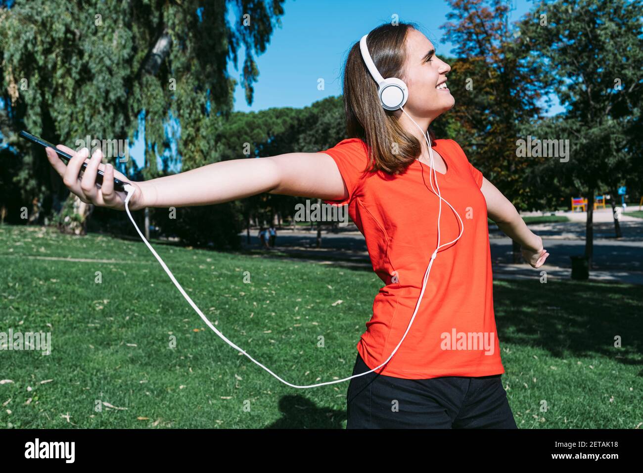 Young blonde wearing a red shirt feels free listening to music with headphones on in a park Stock Photo