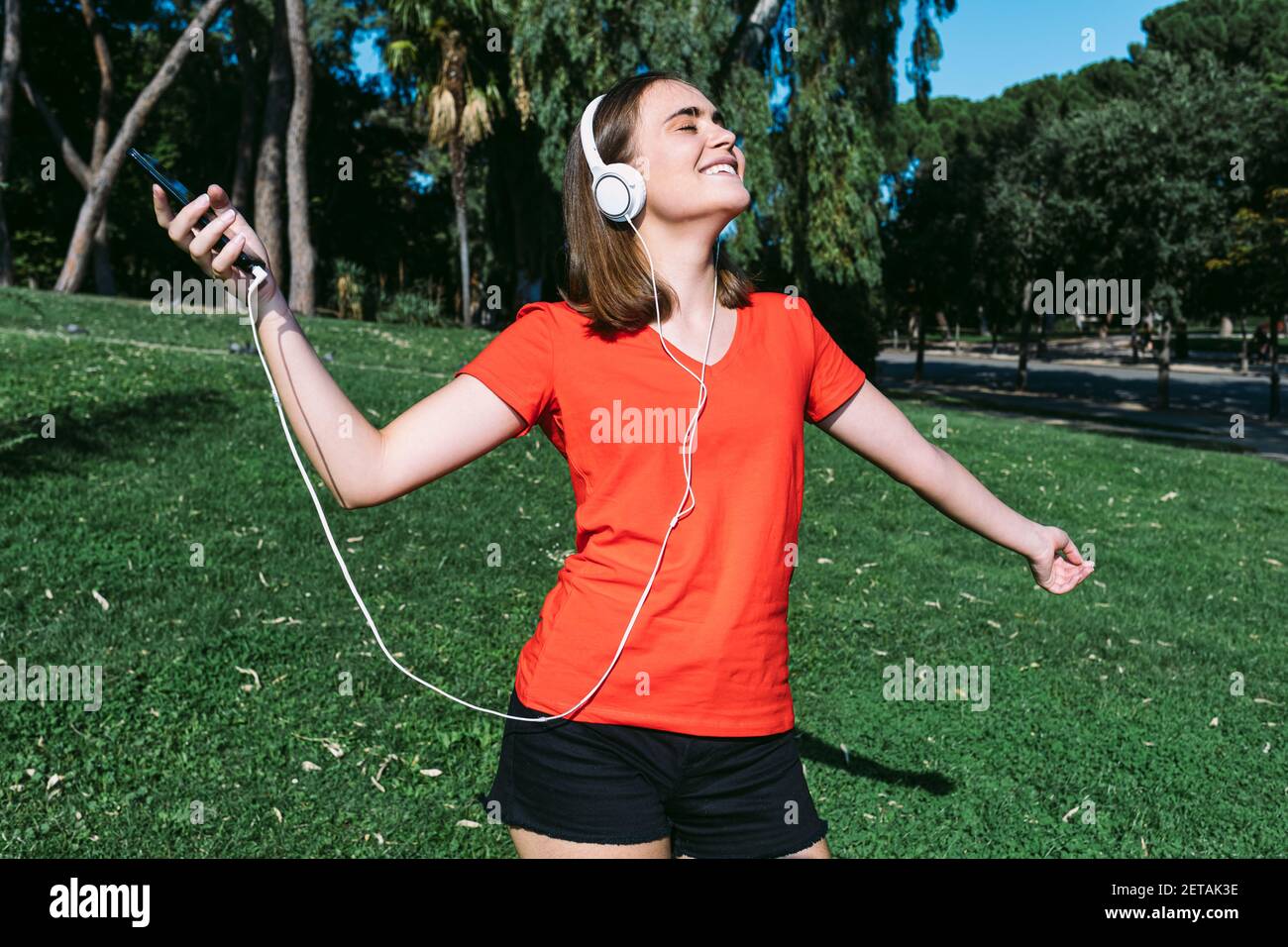 Young blonde wearing a red shirt feels free listening to music with headphones on in a park Stock Photo