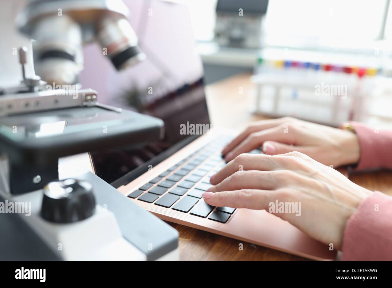 Female hands are working on laptop next to microscope Stock Photo