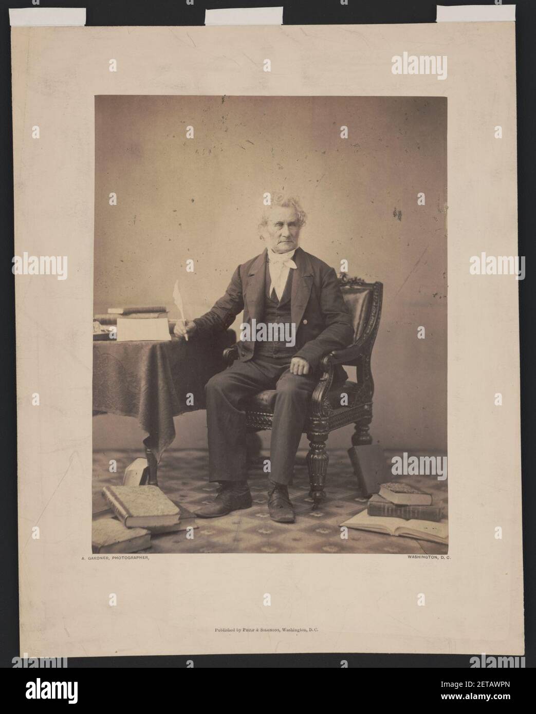 Peter Force, full-length portrait, seated at table, facing slightly right, holding a quill pen in his right hand, with books on table and floor) - A. Gardner, photographer, Washington, D.C Stock Photo