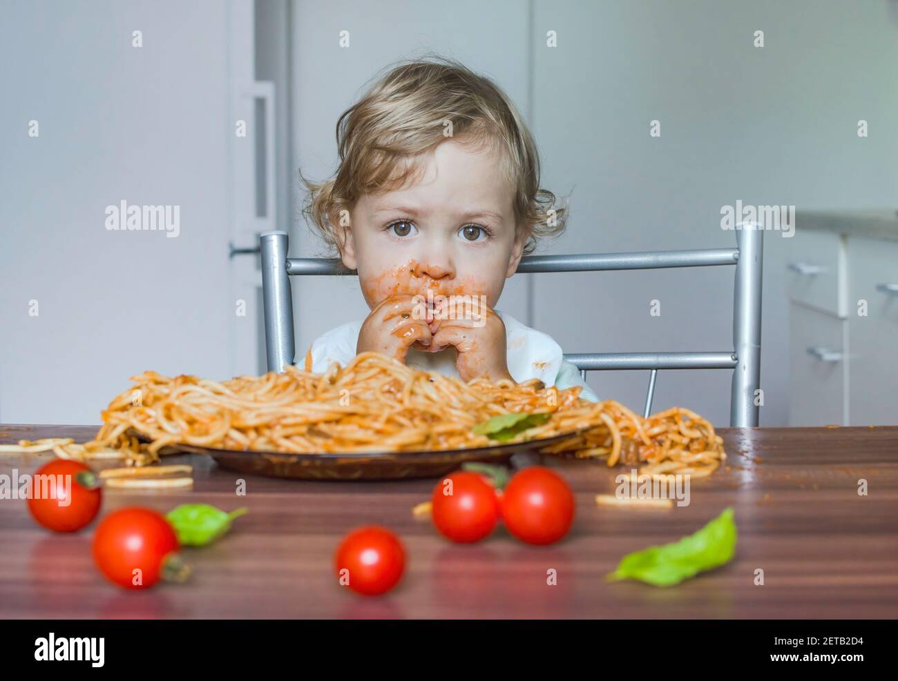 Funny baby child getting messy eating spaghetti with tomato sauce from