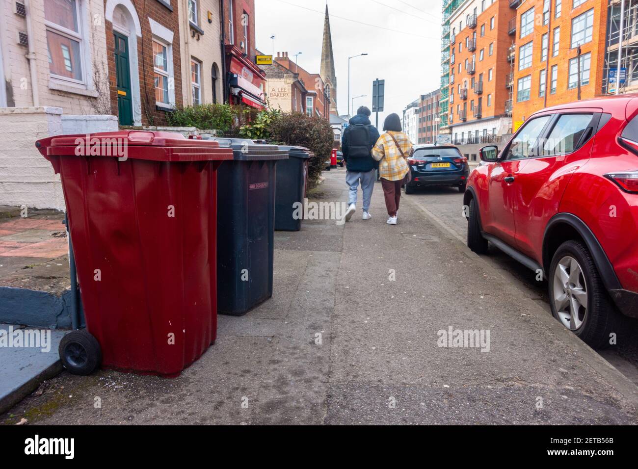 Read recycling and black general waste bins left of the pavement ready for collection along a street in Reading, UK. Stock Photo