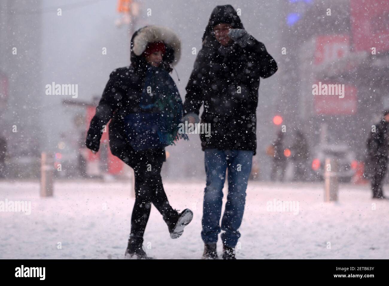 Two people holding hands walk through Times Square during a winter snow