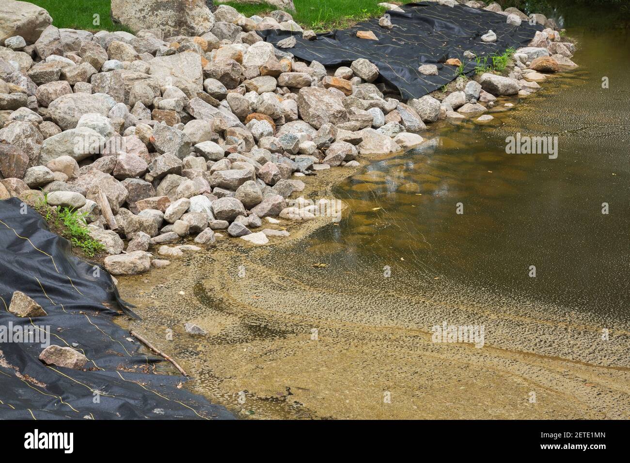 Black polypropylene liner and decorative rocks at edge of large ornamental pond under construction Stock Photo