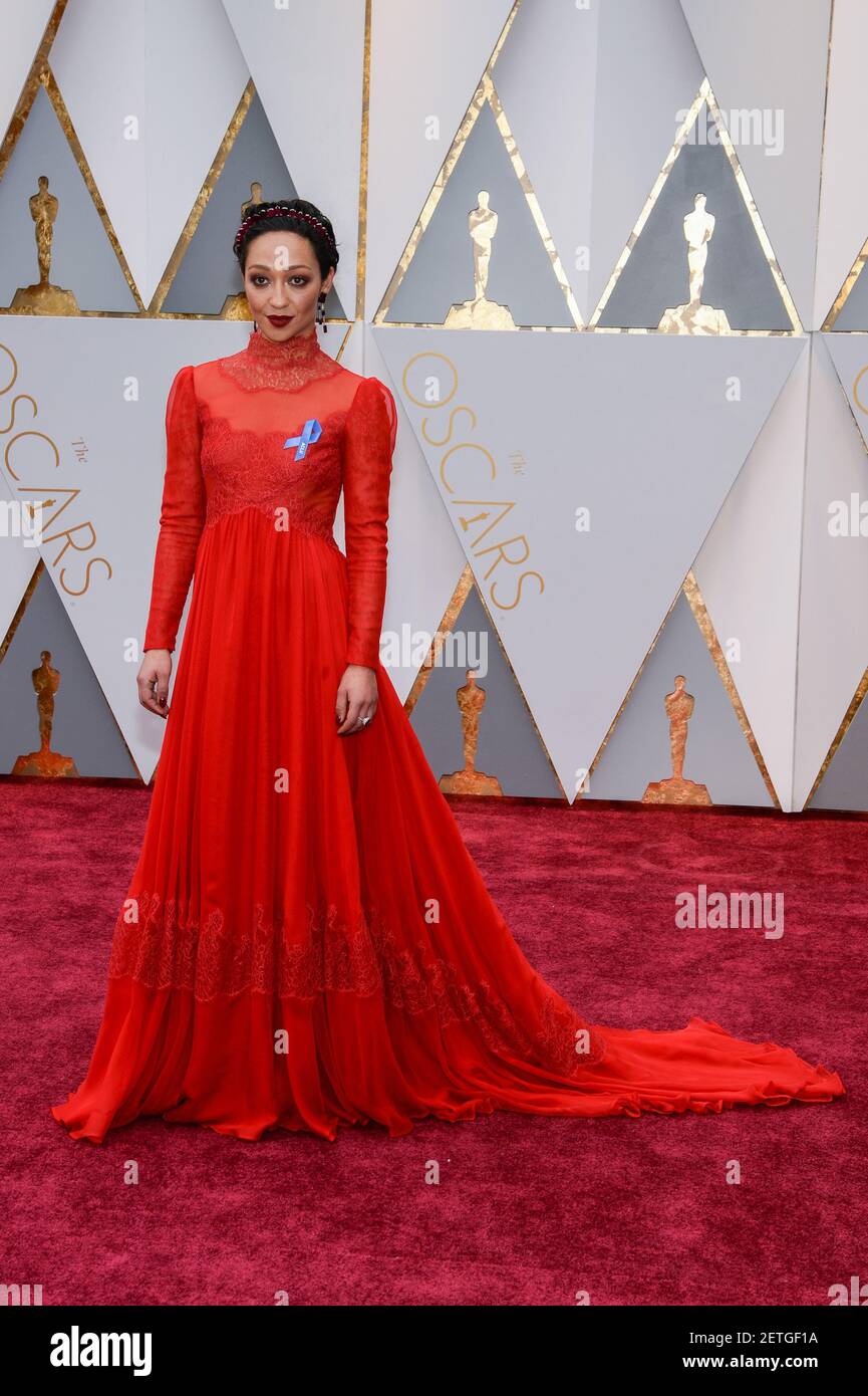 Ruth Negga wearing a red Valentino lace dress with an Irene Neuwirth crown  and earrings and an ACLU blue ribbon walking the red carpet during the 89th  Academy Awards ceremony, presented by