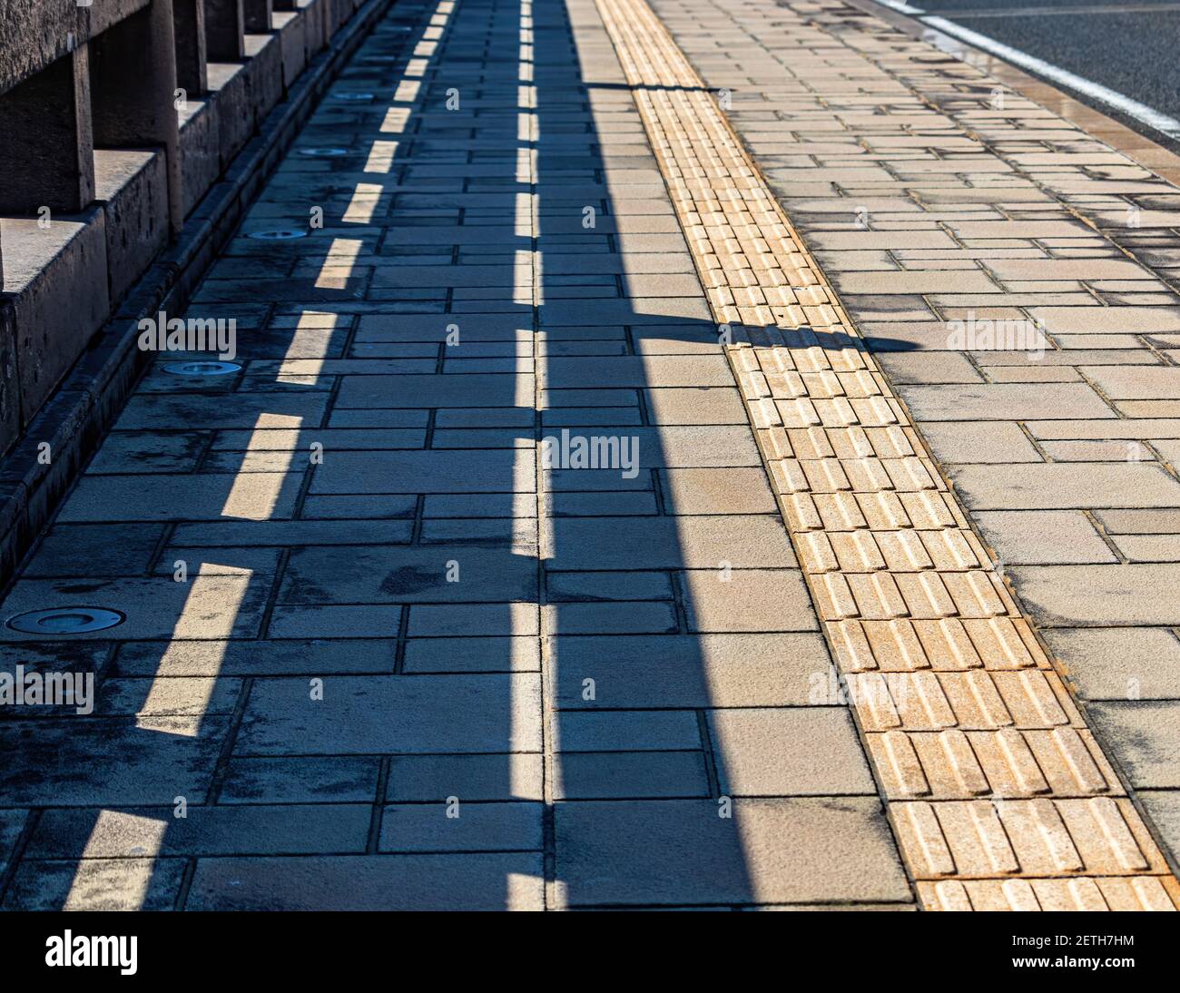 The shadow of a steel railing is cast onto the pavement of a bridge ...