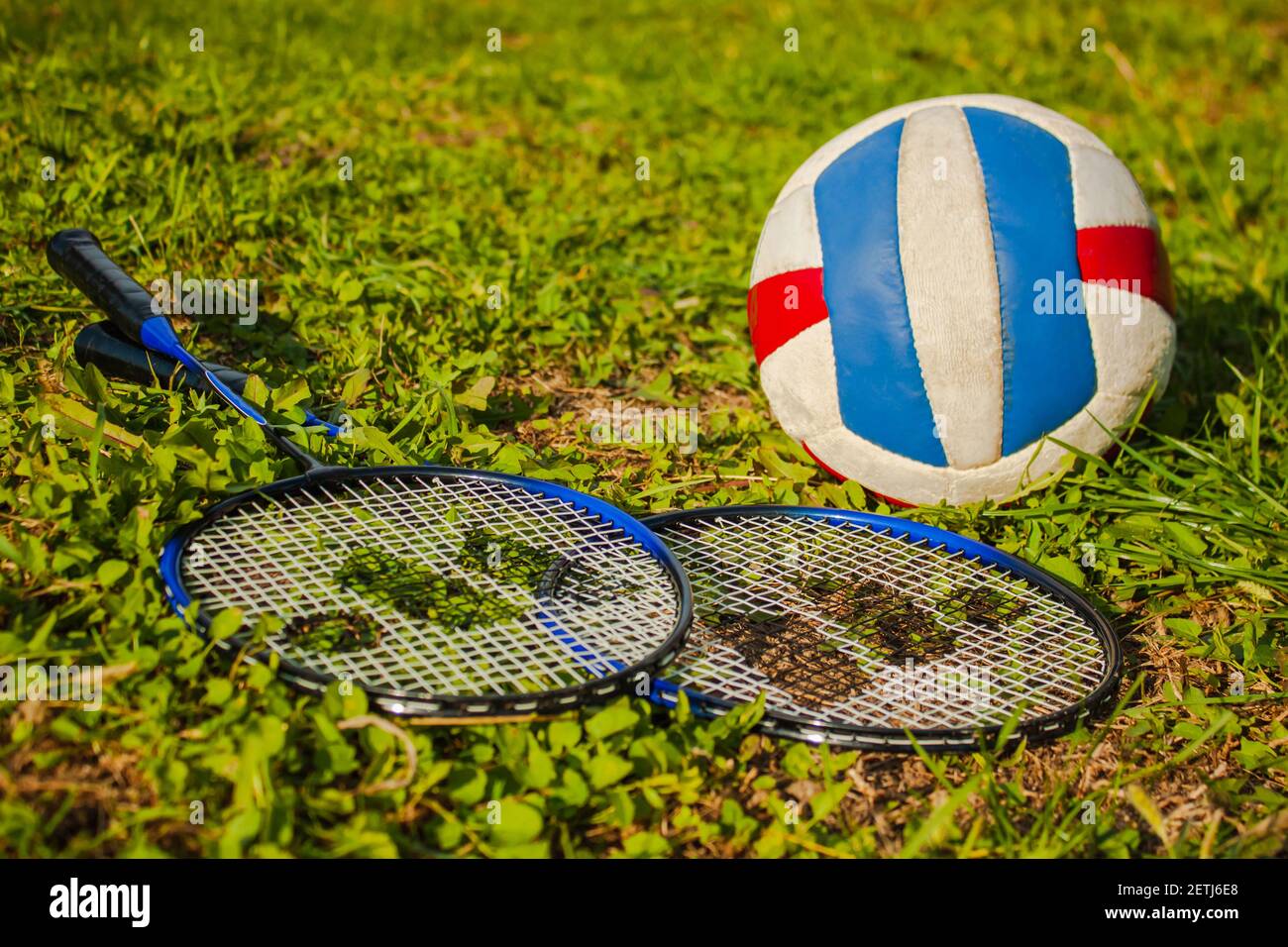 An old volleyball ball and two badminton rackets are lying on the grass ...