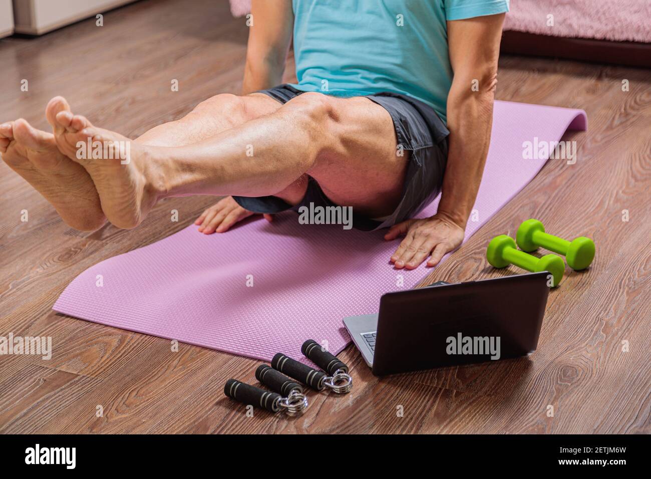 50-year-old man performs exercises while lying on the rug at home, looking at the computer. During a pandemic, a person trains in an apartment via the Stock Photo