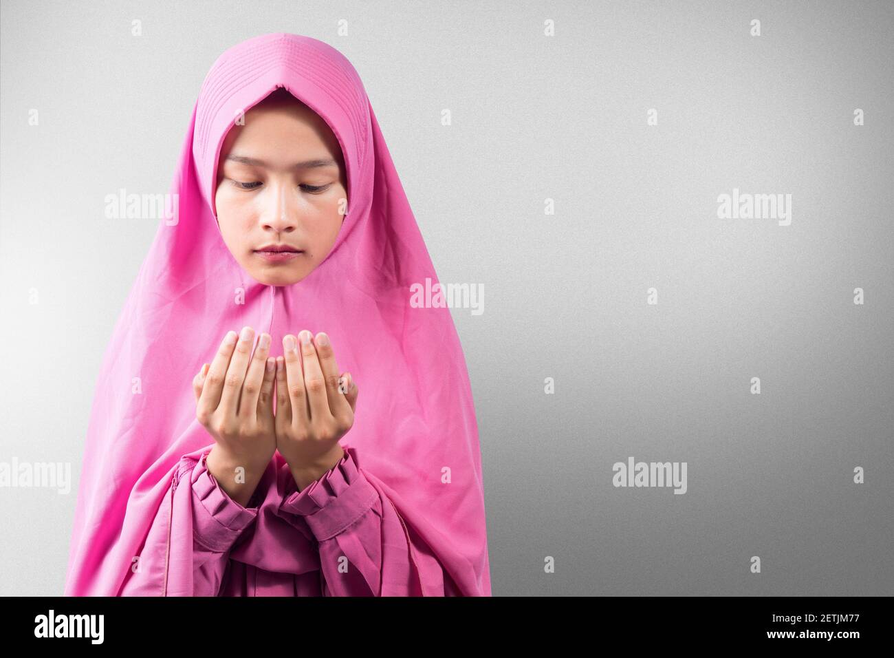 Asian Muslim woman in a veil standing while raised hands and praying ...