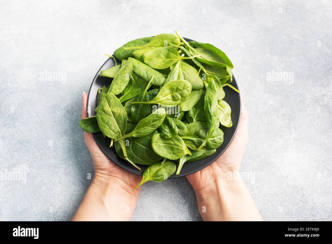 Spinach green fresh leaves on a black plate. Female hands holding a plate Stock Photo