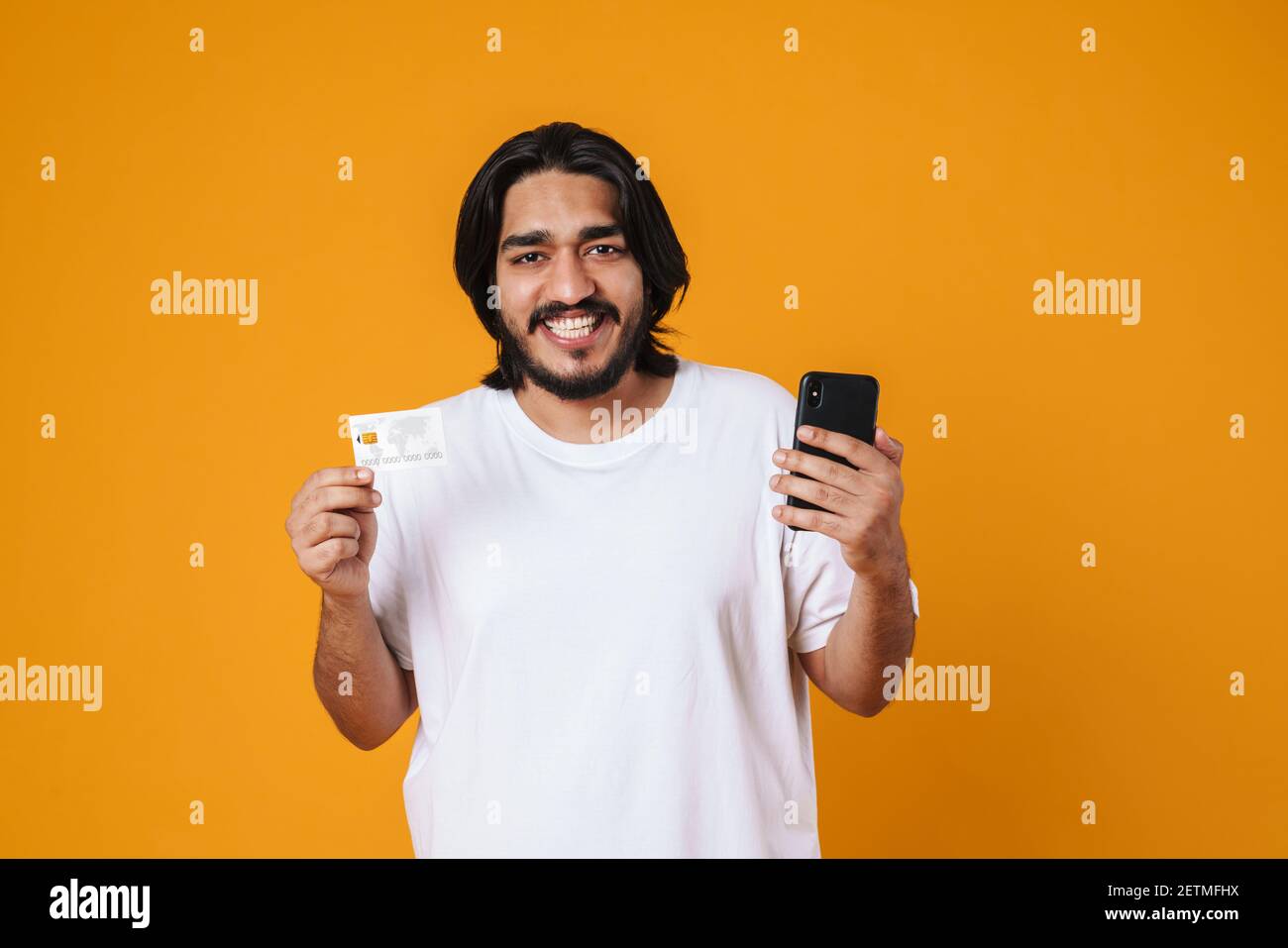 Happy indian man showing mobile phone and credit card isolated over ...