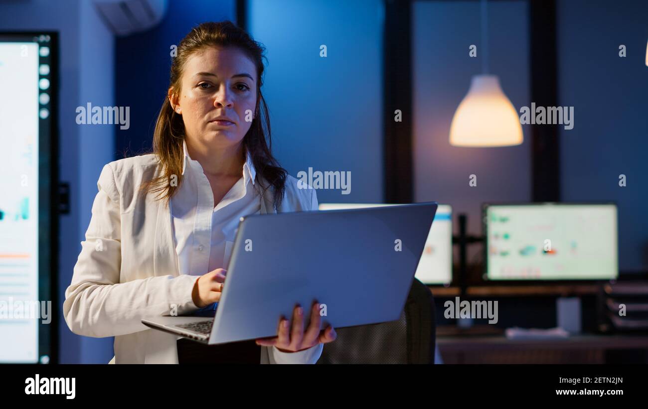 Staff Using Technology Tired manager raising head looking at camera sighing holding laptop ...