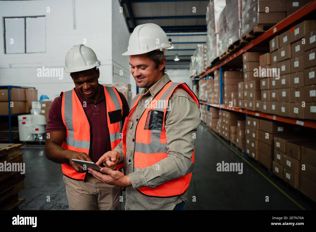 Two workers smiling while looking at photos on digital tablet laughing in warehouse store Stock Photo