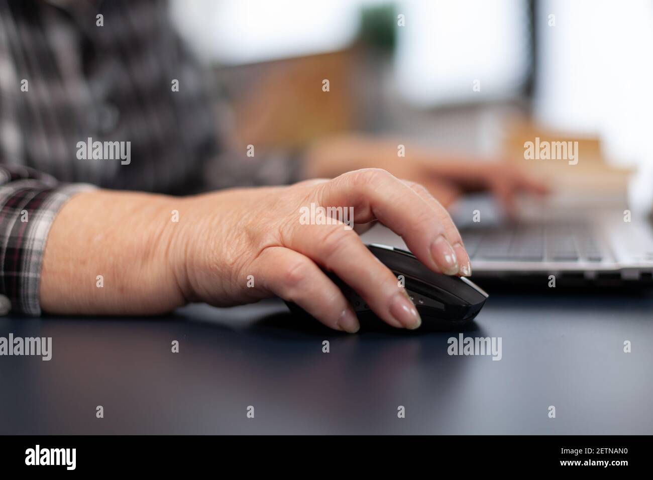 Close up of old entrepreneur lady using mouse in home office. Elderly woman in home living room using moder technoloy laptop for communication sitting at desk indoors. Stock Photo