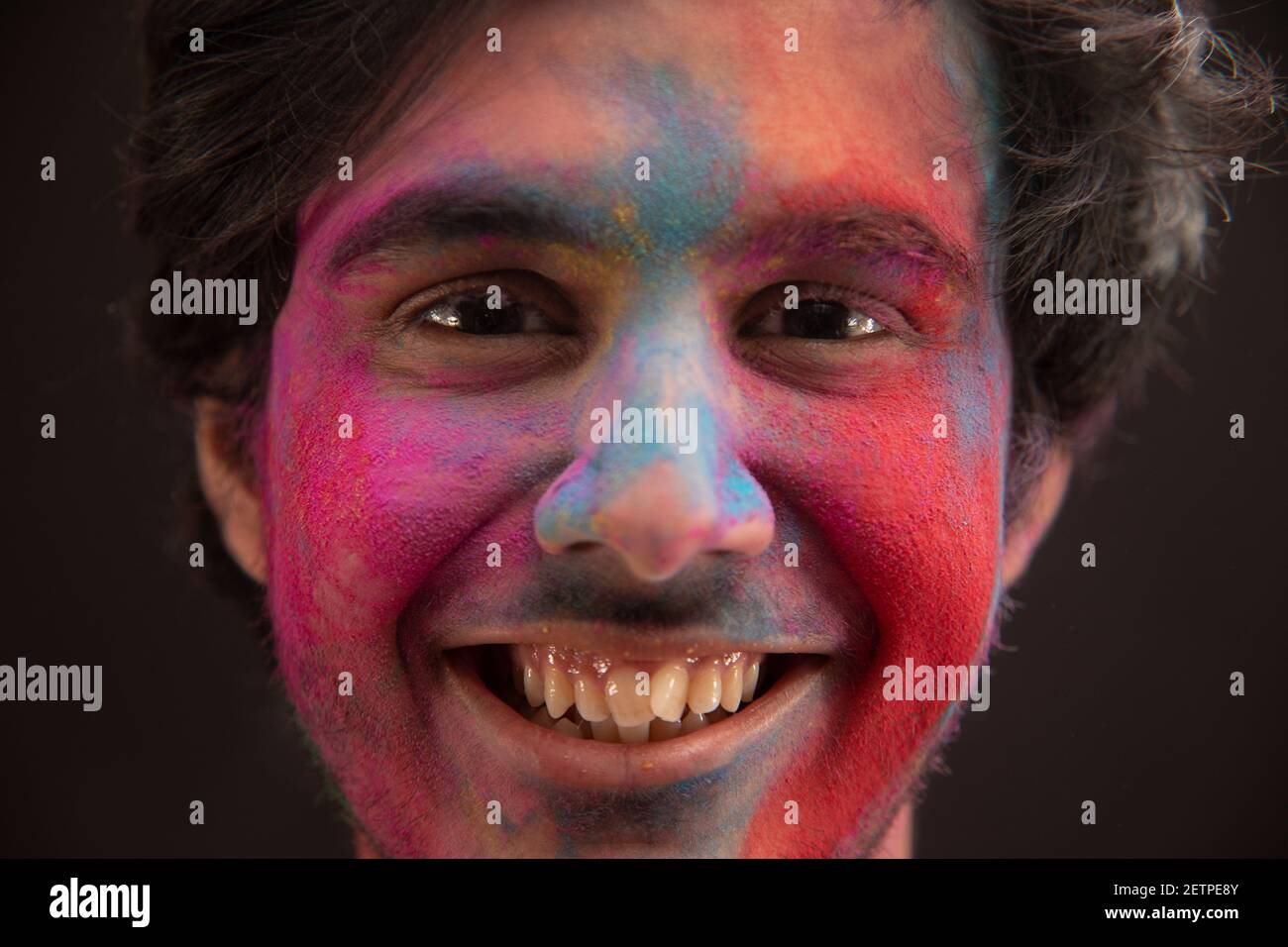 PORTRAIT OF A HAPPY YOUNG MAN WITH GULAL ON HIS FACE LOOKING AT CAMER AND SMILING Stock Photo